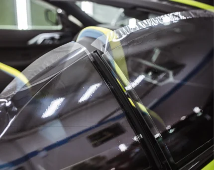 Clear protective film being carefully applied to the top edge of a car door window.