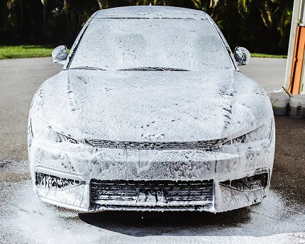 White sedan completely covered in thick white foam during a car wash.