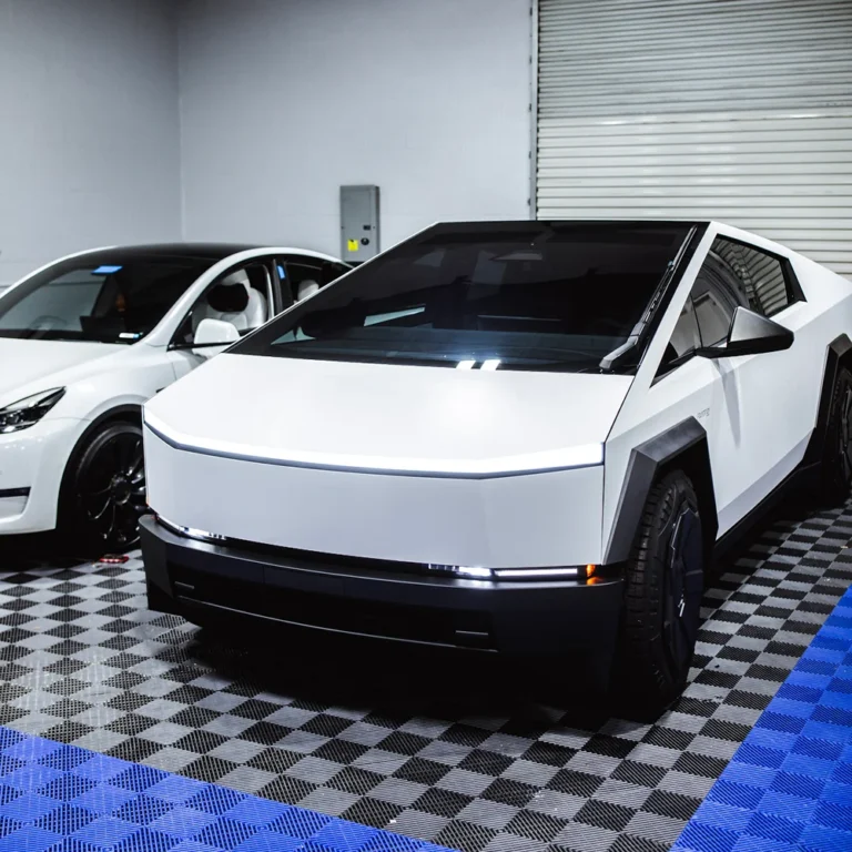 White Tesla Cybertruck parked indoors on a checkered floor next to a white Tesla Model X.