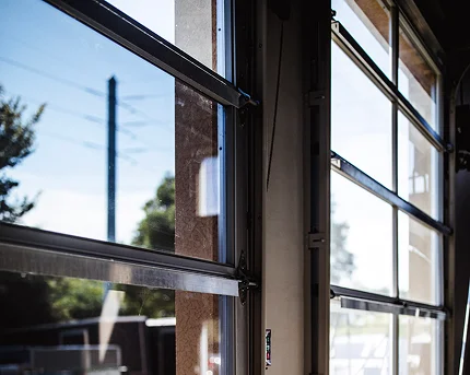 Sunlight shining through partially opened glass-paneled garage doors, revealing a view of trees and blue sky outside.