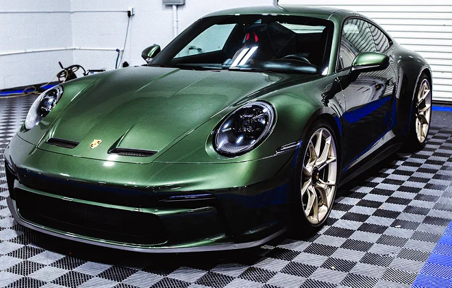 Metallic green Porsche sports car with gold wheels parked indoors on a checkered garage floor.