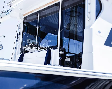 Close-up of a yacht's glass cabin windows reflecting the marina, with visible seating and control equipment inside.