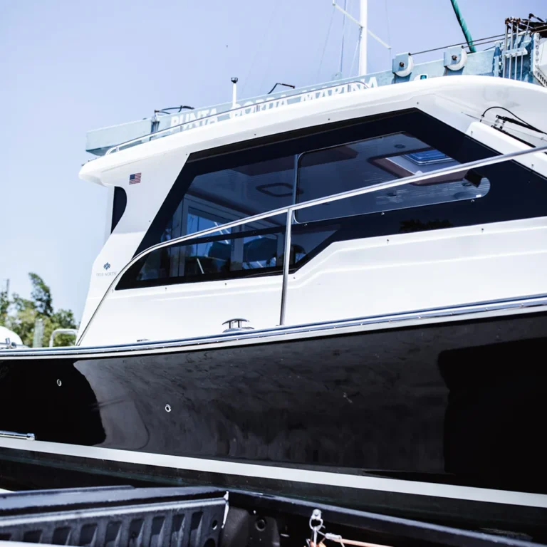 Side view of a black and white cabin cruiser boat with reflective tinted windows, docked near a truck bed at Punta Gorda Marina under a clear blue sky.