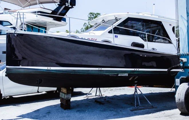 Black and white cabin cruiser boat propped on stands in a marina repair area with other yachts in the background.