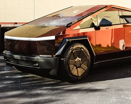 Glossy copper-colored Tesla Cybertruck parked on asphalt, reflecting its surroundings with its angular design and matching metallic wheels.
