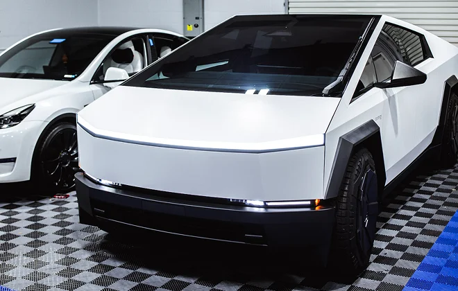 White Tesla Cybertruck with a matte finish parked indoors beside another Tesla, showcasing its angular design and dark-tinted windows.