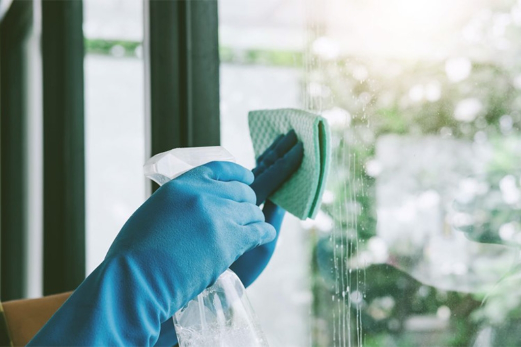 Close-up of a person wearing blue gloves cleaning a commercial window in Fort Myers with a spray bottle and soft cloth, illustrating proper care as part of maintenance and longevity tips for window tinting.