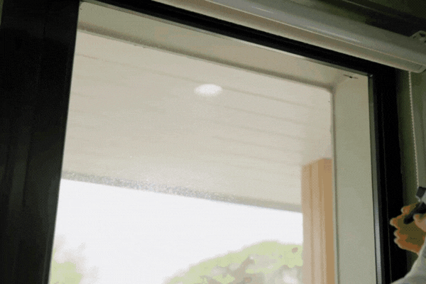 Close-up of a person spraying cleaner on a tinted glass door and wiping it down inside a Fort Myers home to maintain and clean tinted home windows.