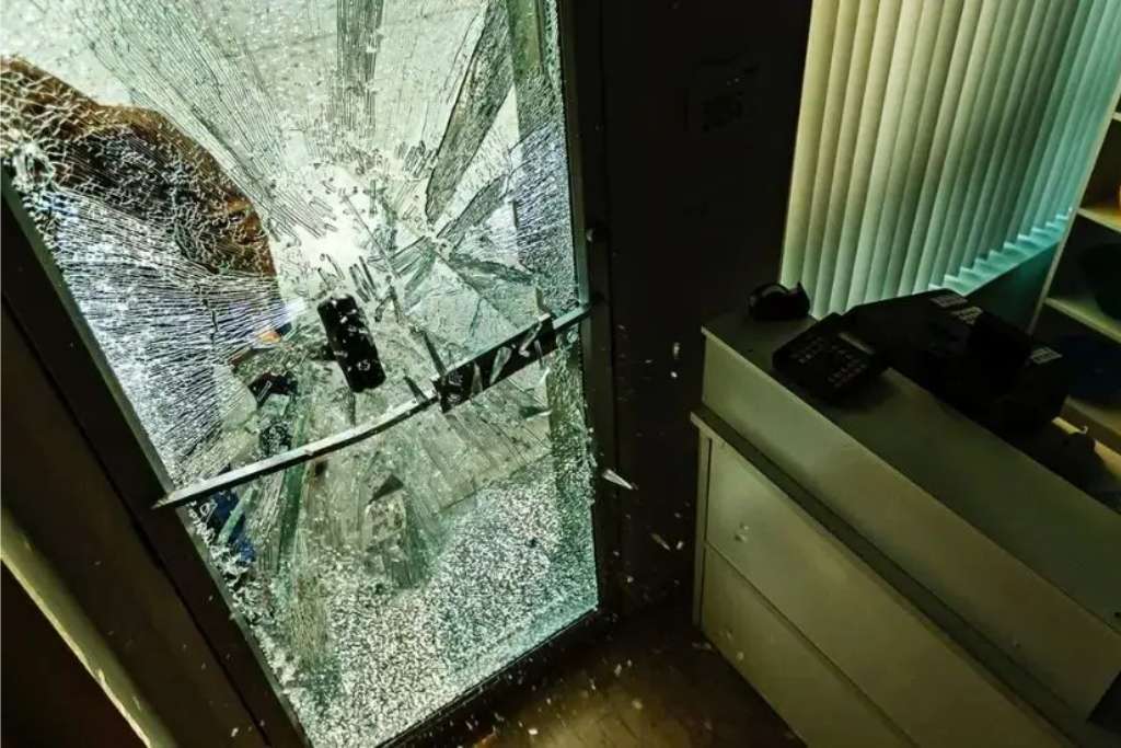 A shattered glass door inside a commercial space shows extensive damage from an attempted break-in, yet the glass remains mostly intact due to security window film. This image illustrates the real-world benefits of security window film in preventing forced entry and minimizing injury risks.