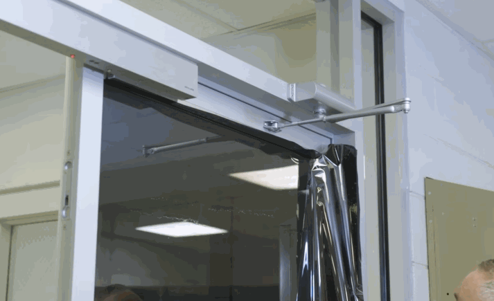 A technician carefully applies a dark tinted film to a glass door inside a commercial building using precise tools.