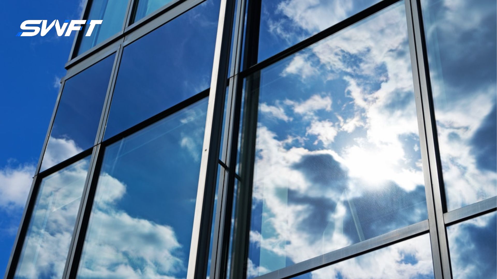 A modern commercial building with large tinted glass windows reflecting a bright blue sky and clouds, with the SWFT logo in the top left corner.